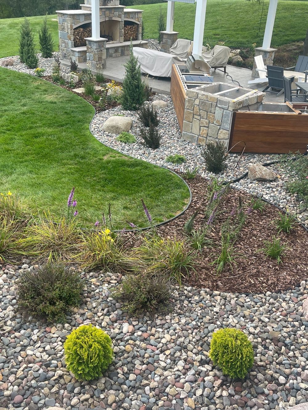 Landscaped garden featuring stone patio, plants, shrubs, and decorative stone borders.